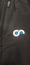 Load image into Gallery viewer, Close-up of a black shorts with a logo on the leg area with zip.
